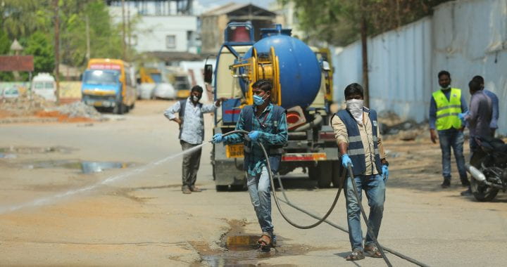 Photo of men in masks spraying a street in Hyderabad, India